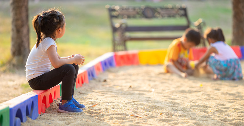 Little girl sitting lonely watching friends play at the playground.The feeling was overlooked by other people. Concept child shy