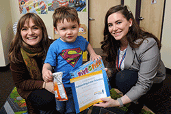 Child and mother smile for photo after participating in research. The child holds a certificate of completion and a prize.